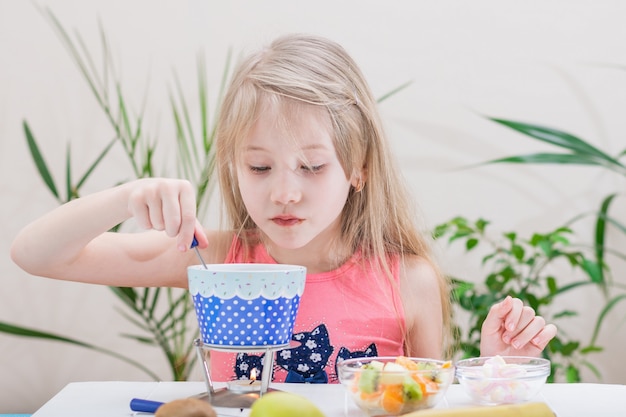 Petite fille prépare et mange une fondue au chocolat.