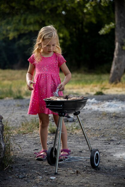 Photo une petite fille prépare de la viande de poulet barbecue à l'extérieur dans le parc dans la nature