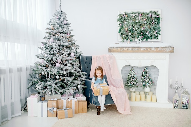 Petite fille près d'un arbre de Noël avec des jouets, à côté d'une cheminée