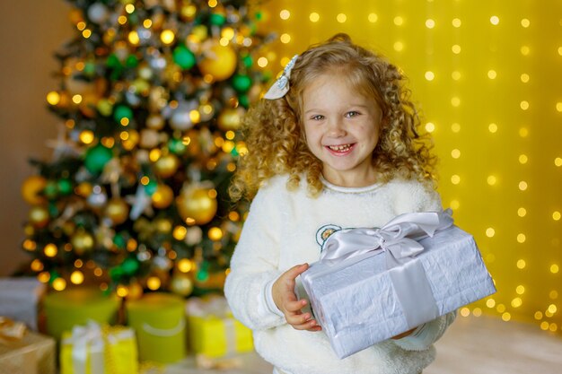 Petite fille près de l'arbre de Noël tenant un cadeau souriant