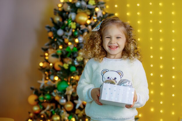 Petite fille près de l'arbre de Noël tenant un cadeau souriant