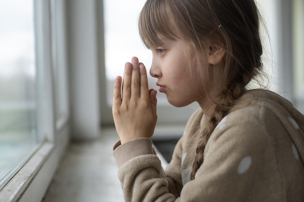 Petite fille priant près de la fenêtre.