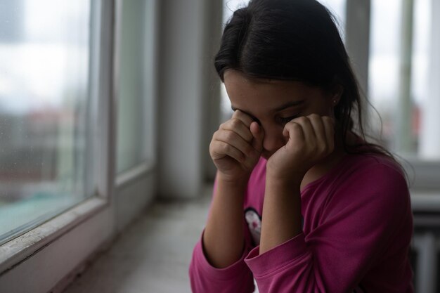 Petite fille priant près de la fenêtre.