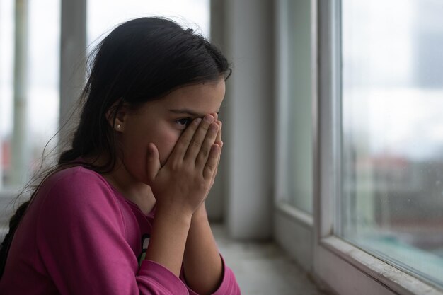 Petite fille priant près de la fenêtre.