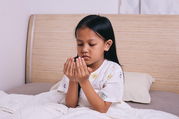 Une petite fille prie dans sa chambre avant de dormir.