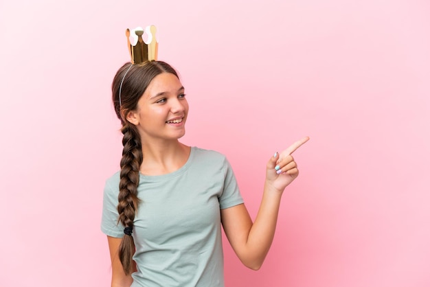 Photo petite fille princesse caucasienne isolée sur fond rose pointant le doigt sur le côté et présentant un produit