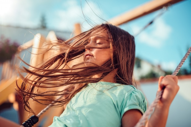 Petite fille profitant de la balançoire avec les yeux fermés et les cheveux longs volant