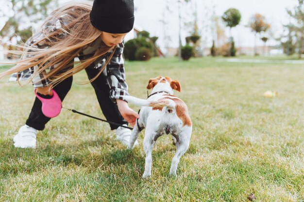 Une petite fille promène son chien dans un parc de la ville un enfant joue avec un terrier Jack Russell à l'extérieur Le concept de soins pour animaux de compagnie