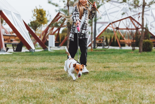 Une petite fille promène son chien dans un parc de la ville un enfant joue avec un terrier Jack Russell à l'extérieur Le concept de soins pour animaux de compagnie