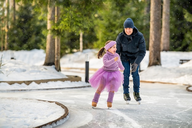 Petite fille en pull rose et jupe ample monte sur une journée d'hiver ensoleillée sur une patinoire extérieure dans le parc