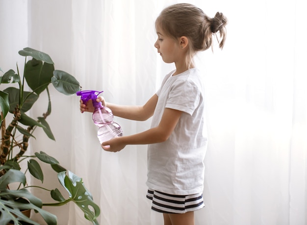Petite fille pulvérisant des feuilles de plantes d'intérieur, prenant soin de la plante Monstera.