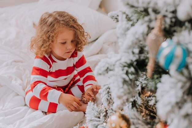 Petite fille en pyjama rayé de Noël décore le sapin de Noël. mode de vie. Photo de haute qualité