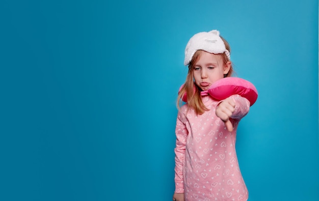 Petite fille en pyjama rose et avec un oreiller de couchage malheureux mauvais sommeil