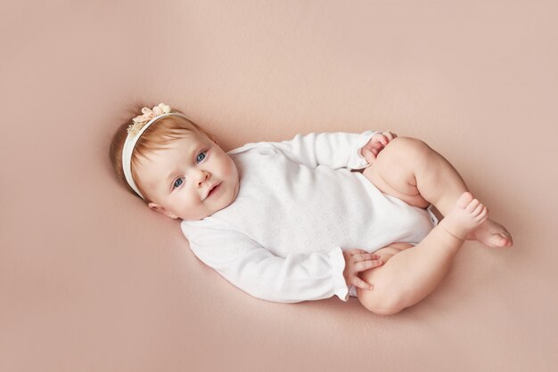 Petite fille de quatre mois se trouve sur un mur rose pâle