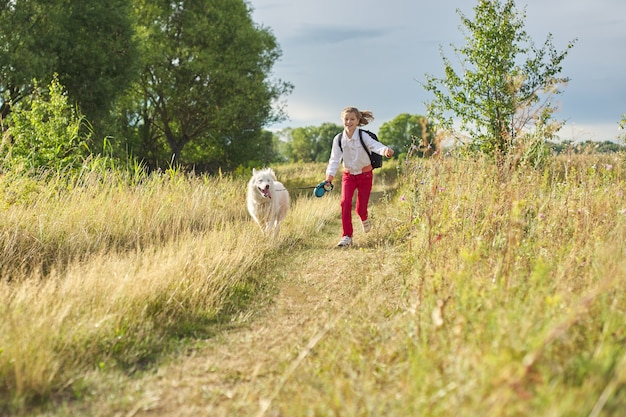 Petite fille qui court avec un chien dans le pré.