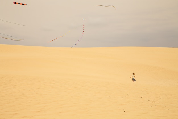 Petite fille qui court vers une zone où les cerfs-volants volent dans les dunes de sable d'une plage