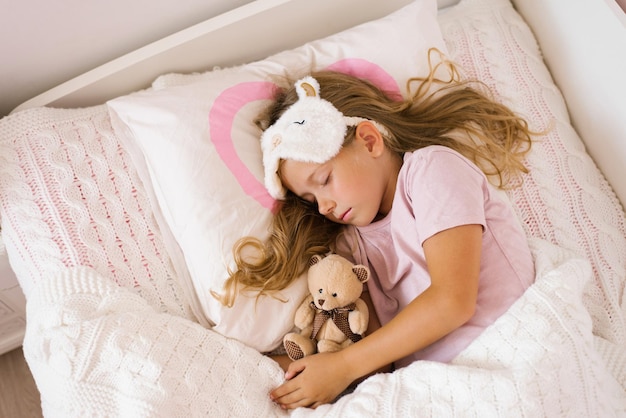 Une petite fille qui dort avec une peluche dans son lit sur un oreiller est un doux sommeil calme d'un enfant