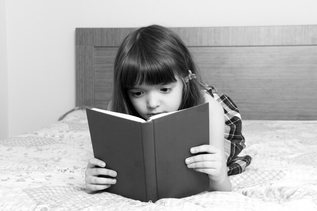 Une petite fille qui lit un livre à la maison.