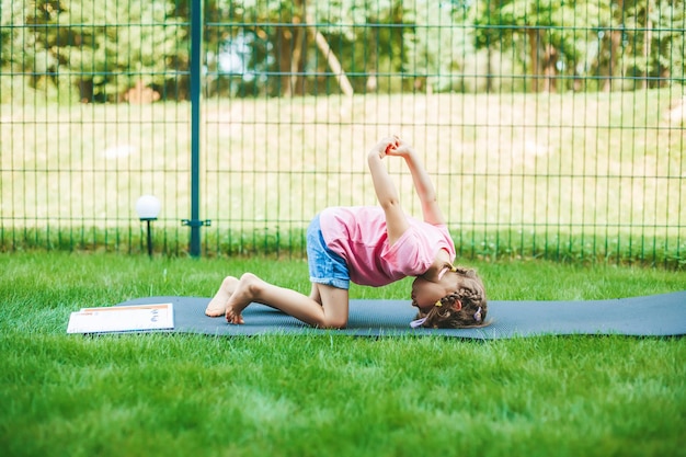 Petite fille qui s'étend sur le tapis roulant pratiquant le yoga à l'extérieur Yoga pour enfants Mode de vie sain pour enfants