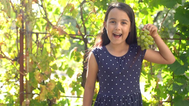 petite fille avec des raisins sourit et montre un tas