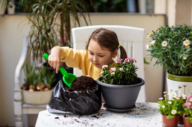 Petite fille ramasser la terre avec une pelle et concentrer la plantation de fleurs dans un pot sur le balcon