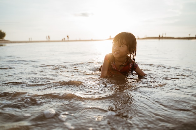 Petite fille ramper sur le sable dans la plage tout en jouant avec de l'eau