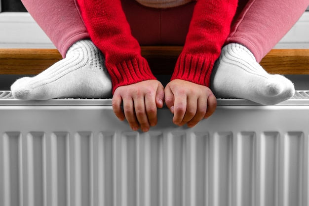 Une petite fille réchauffe ses mains et ses pieds sur un radiateur