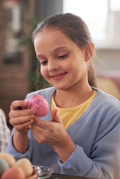 Petite fille regardant l'oeuf de Pâques dans ses mains, elle le peint pour les vacances