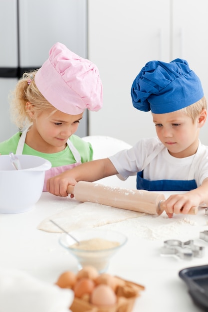 Petite fille en regardant son frère sérieux en utilisant un rouleau à pâtisserie
