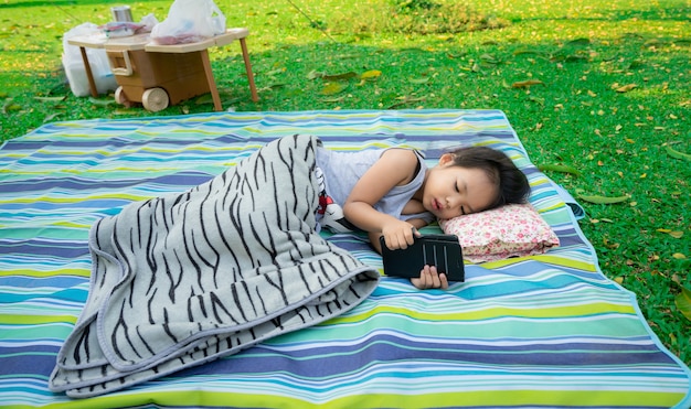 Petite fille en regardant un téléphone portable en position couchée dans le parc