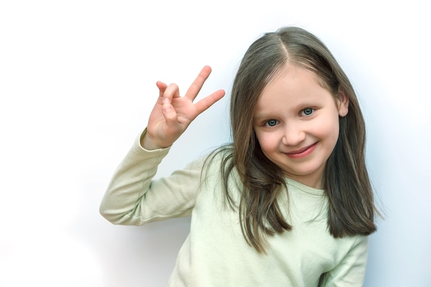 Photo la petite fille regarde la caméra et montre un signe de victoire avec sa main