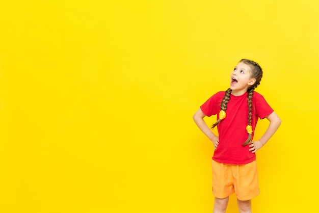 Une petite fille regarde l'espace pour votre publicité isolé jaune Une écolière dans un t-shirt rouge regarde votre annonce dans un espace vide