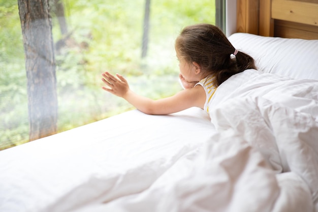 Une petite fille regarde par la fenêtre donnant sur la forêt Glamping Hotel Détendez-vous seul avec la nature Espace pour le texte