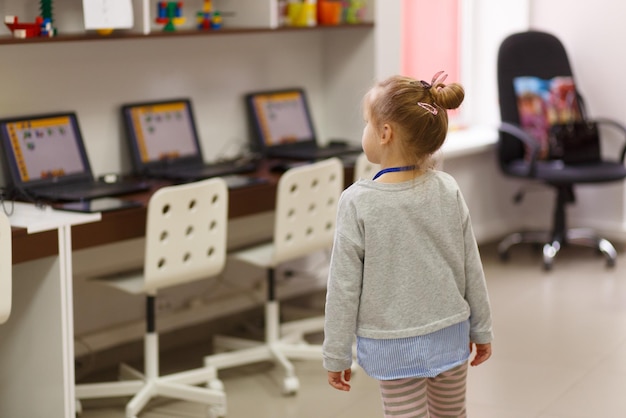 Une petite fille regarde une table avec des ordinateurs portables dans un centre éducatif pour enfants