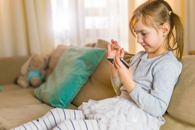 La petite fille regarde le téléphone portable. fille jouant avec un téléphone à la maison. Quarantaine face au coronavirus