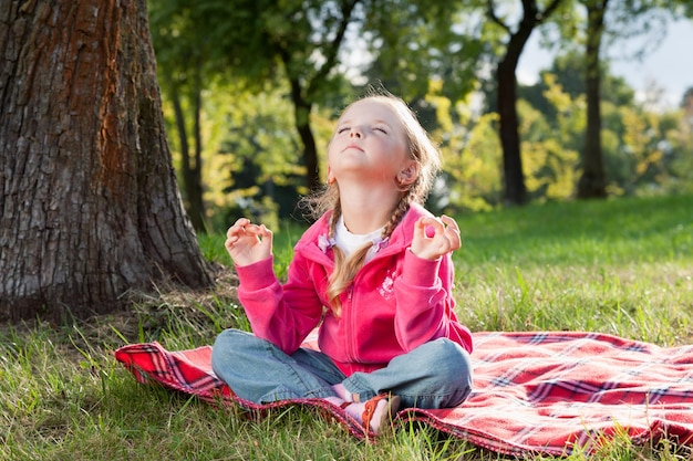 Petite fille relaxante dans la pose de yoga sur l'herbe dans un parc