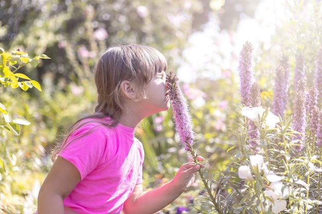 Une petite fille renifle une fleur violette dans le parc