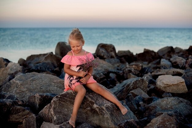 petite fille rêvant sur une pierre sur la plage