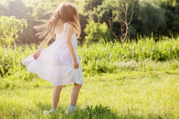 Une petite fille en robe blanche danse sur l'herbe au bord de la rivière