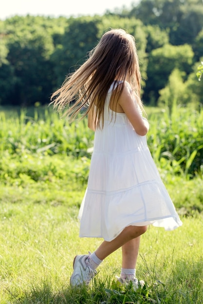 Une petite fille en robe blanche danse sur l'herbe