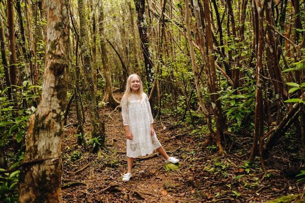 Une petite fille en robe blanche se promène dans la jungle sur une île tropicale