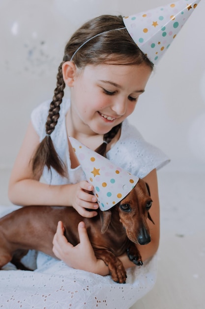 Petite fille en robe blanche avec son teckel de chien bien-aimé dans ses bras fête son anniversaire