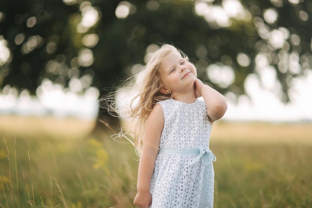 Petite fille en robe bleu ciel debout dans un champ devant un grand arbre