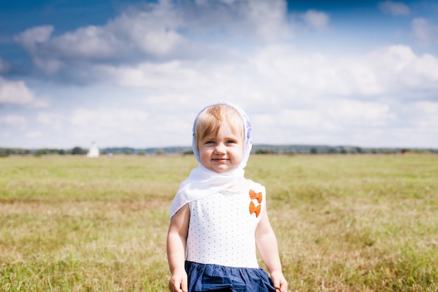 Petite fille en robe et écharpe sur sa tête en champ d'été