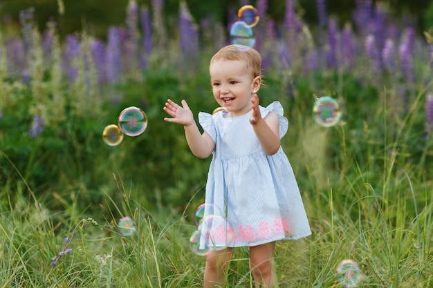 Petite fille en robe essaie d'attraper des bulles de savon