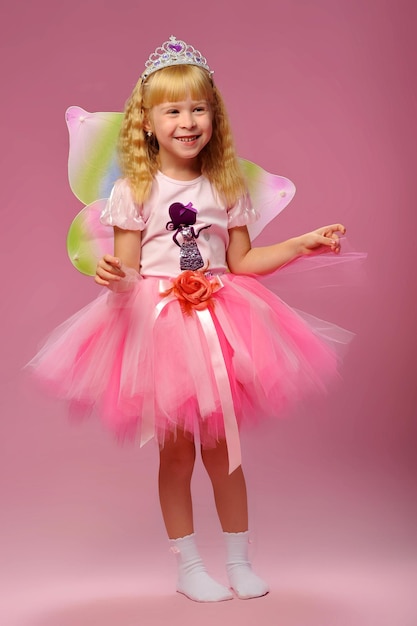 Petite fille en robe de fée avec des poupées sur fond rose