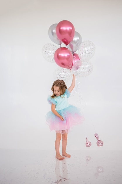 Petite fille en robe de fête se tient avec un tas de ballons sur blanc avec une place pour le texte