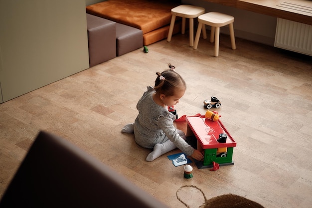 Petite fille en robe grise joue dans la chambre des enfants avec un ensemble de garage et de voitures élégantes et