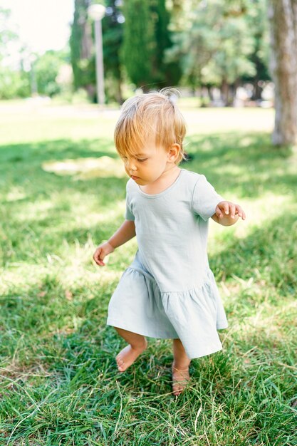 Petite fille en robe marche sur une pelouse verte en regardant ses pieds