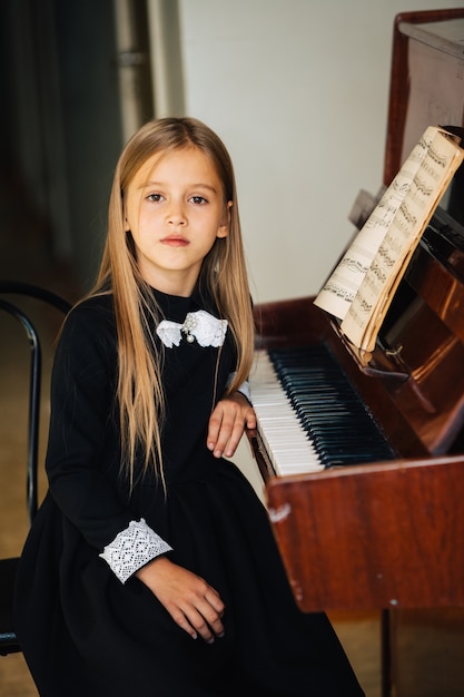 Petite fille en robe noire apprend à jouer du piano. L'enfant joue d'un instrument de musique.